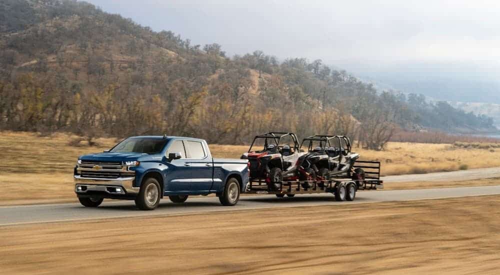 A blue 2020 Chevy Silverado 1500, popular among Chevy Trucks in Albany, NY for sale, is towing 2 side by sides.