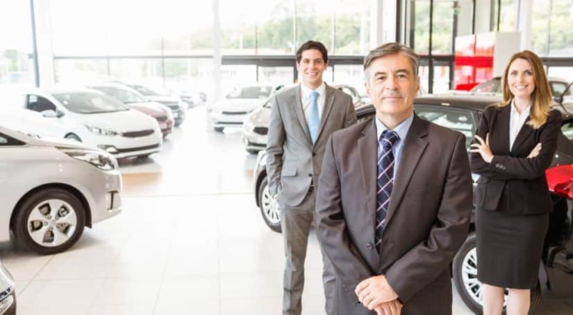 A group of smiling sales people are standing in the showroom of a dealership in Chicago.