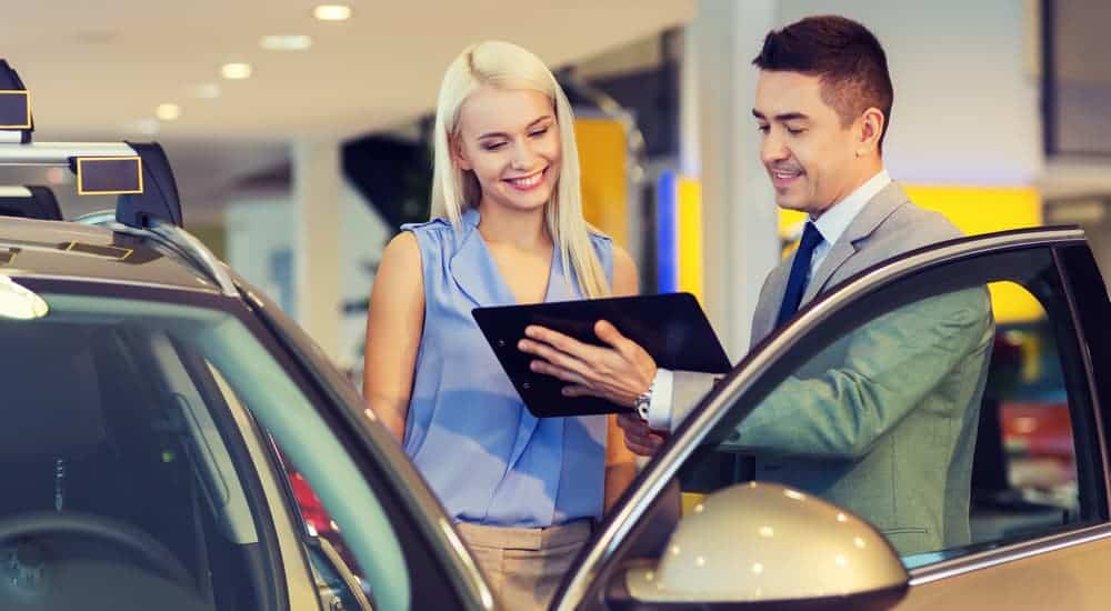 A salesman is helping a smiling customer, which you'll find when you search, "used car dealership near me", decide on her new car.