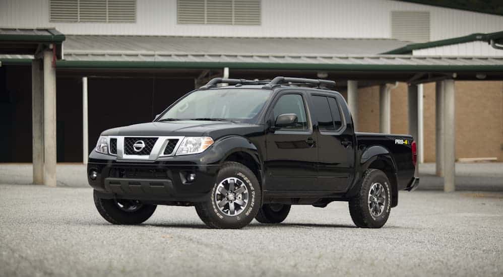 A black 2016 Nissan Frontier is parked in an empty parking lot in front of a building. 