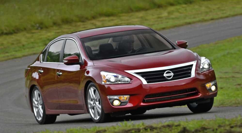 A red 2014 Nissan Altima is driving on a curved road.
