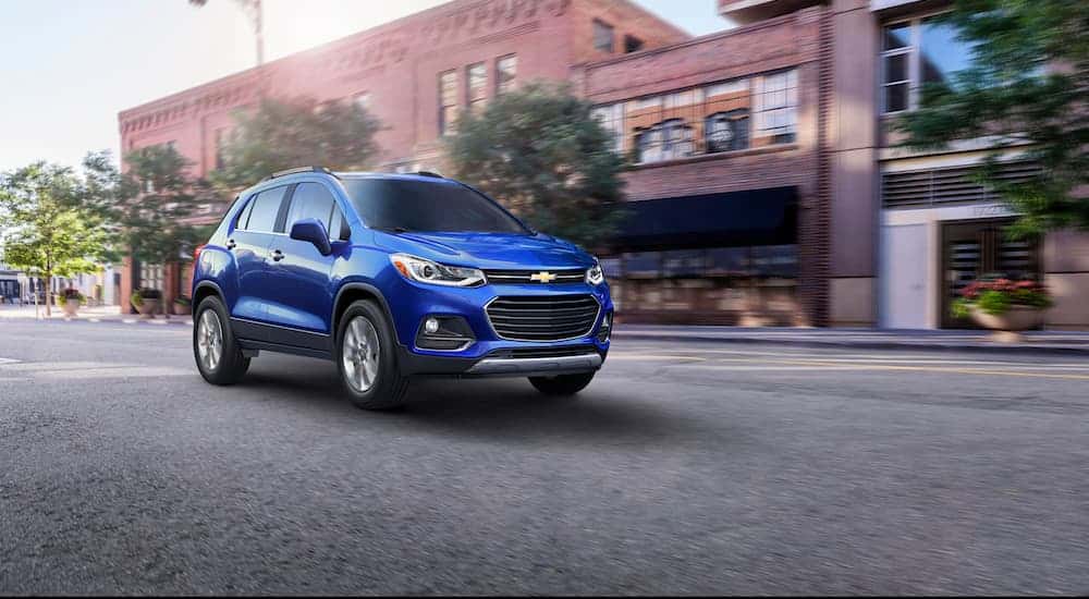 A blue 2017 Chevy Trax, which is a reliable used vehicle you could buy for your New Year's Resolution, is driving on a city street. 