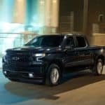 A black 2019 Chevy Silverado 1500 is driving down a lit up city street at night.