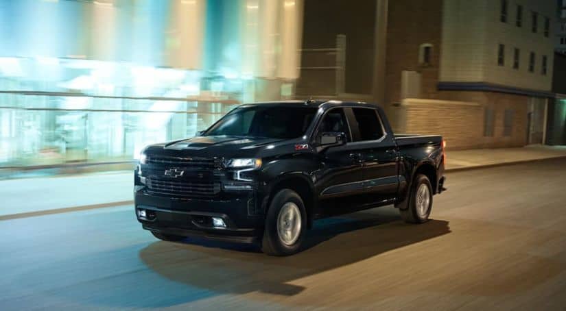 A black 2019 Chevy Silverado 1500 is driving down a lit up city street at night.