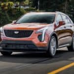 An orange 2020 Cadillac XT4 is driving on a treelined road.