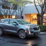 A blue 2020 Cadillac XT5 is parked outside of a house while it's raining.