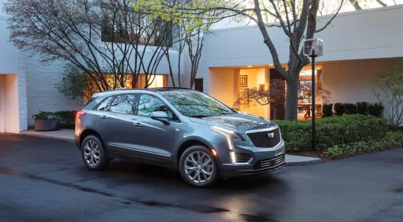 A blue 2020 Cadillac XT5 is parked outside of a house while it's raining.