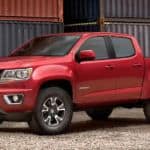 A red 2020 Chevy Colorado is parked next to large metal shipping containers.