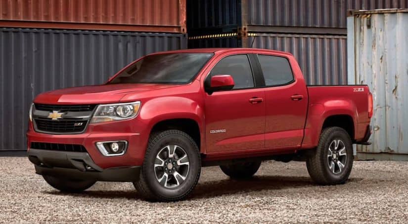 A red 2020 Chevy Colorado is parked next to large metal shipping containers.