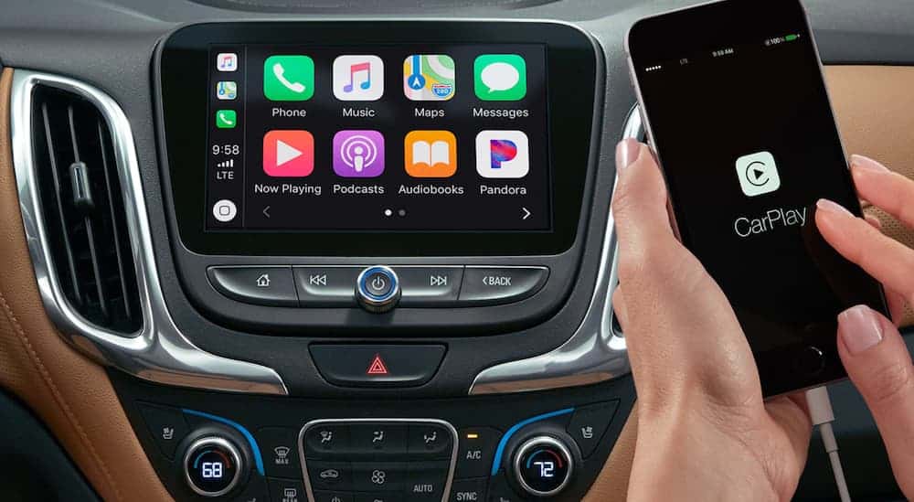 A hand is holding an iPhone that's plugged into the infotainment system of a 2020 Chevy Equinox.