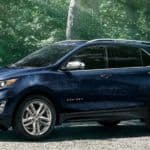 A blue 2020 Chevy Equinox is parked on a dirt path surrounded by trees.