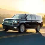A black 2020 Chevy Suburban is driving at sunset with hills in the distance.