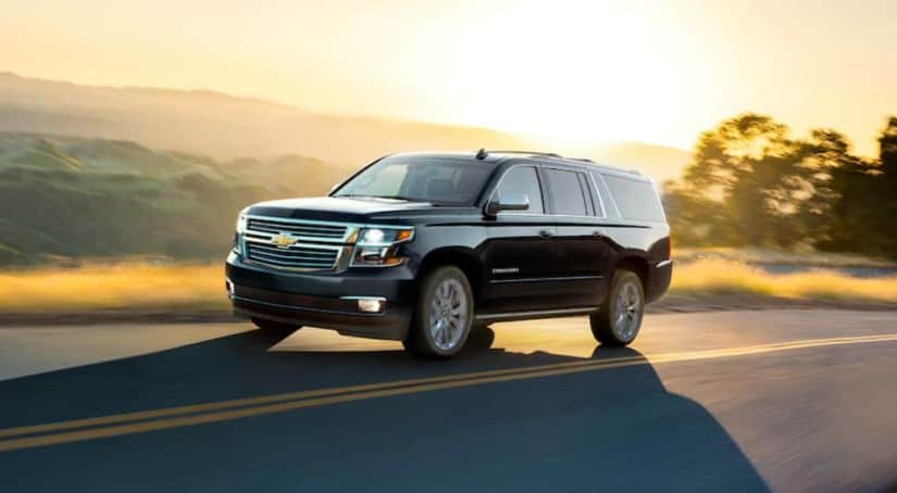 A black 2020 Chevy Suburban is driving at sunset with hills in the distance.