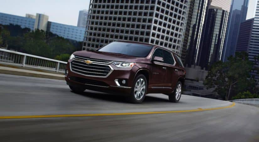 A maroon 2020 Chevy Traverse is driving out of a city.