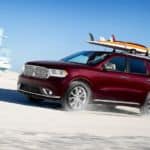 A burgundy 2020 Dodge Durango is driving on the beach with surf boards on top.