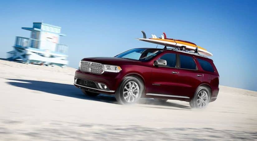 A burgundy 2020 Dodge Durango is driving on the beach with surf boards on top.
