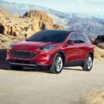 A red 2020 Ford Escape is driving on a dirt road with mountains in the background.