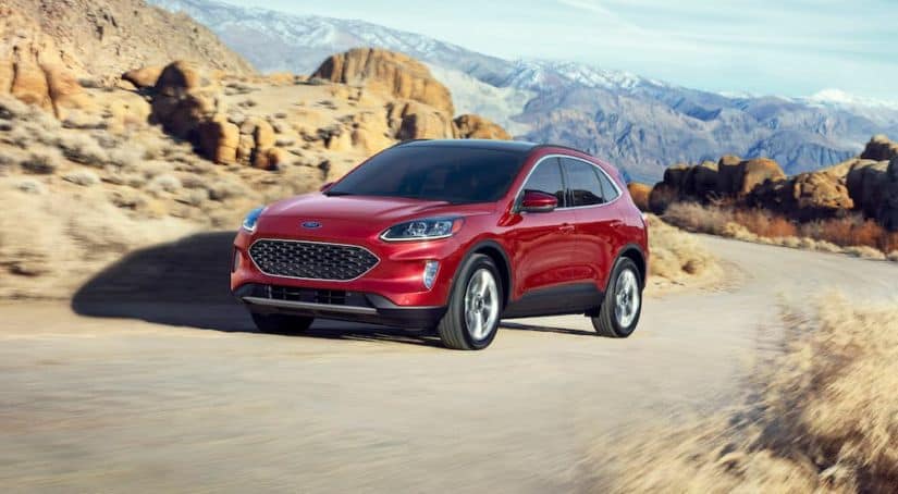 A red 2020 Ford Escape is driving on a dirt road with mountains in the background.