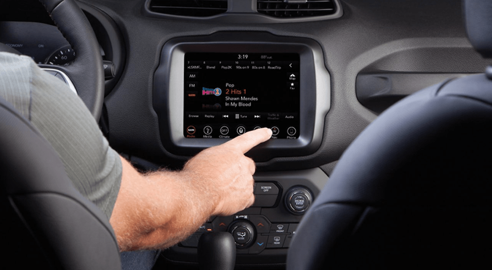 A close up of a hand using the UConnect 8.4-inch touchscreen in a 2020 Jeep Renegade. 