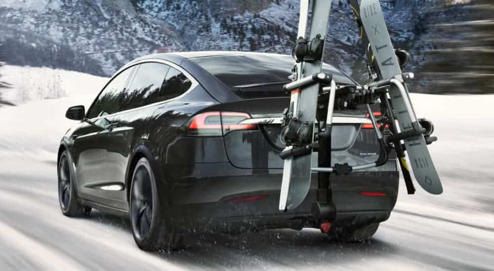 A black 2020 Tesla Model X is carrying skis on a snowy, mountain road.