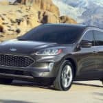 A grey 2020 Ford Escape is driving on a dirt road with mountains in the background.