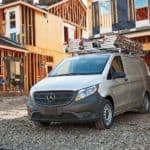 A silver Mercedes-Benz Metris is parked in front of a half built house.