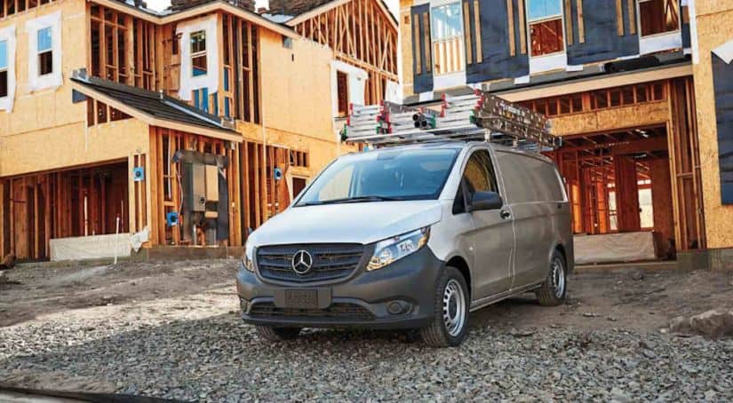 A silver Mercedes-Benz Metris is parked in front of a half built house.
