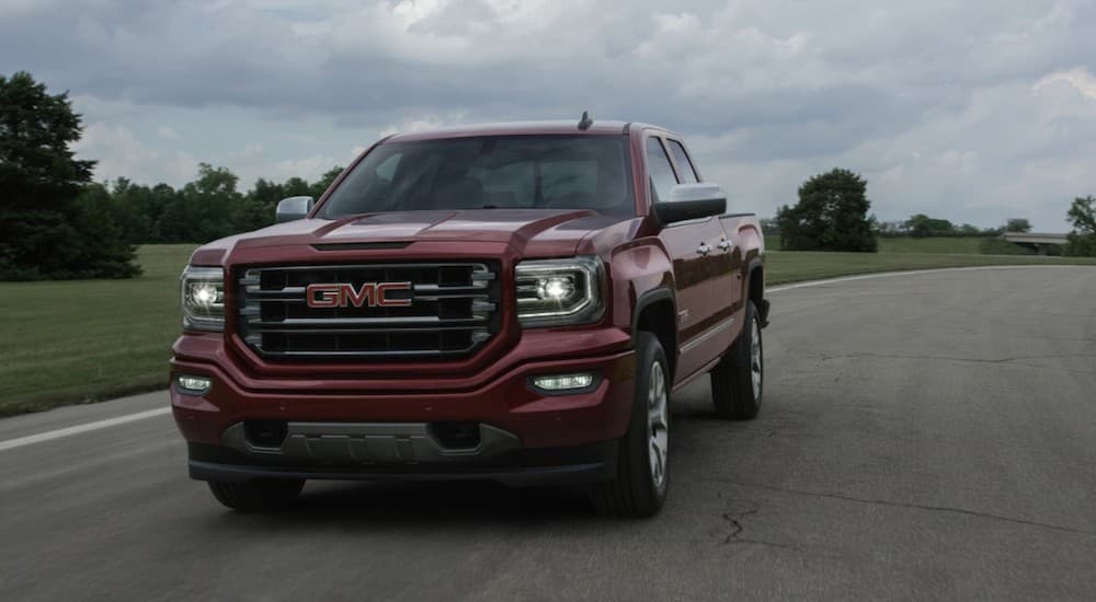 A red 2017 GMC Sierra, similar to the trucks you'll find when looking for Bad Credit Car Dealerships online, is driving on a grass-lined road. 