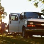 A white Chevy Express van, popular among Chevy vans for sale, is unloading passengers in a park.