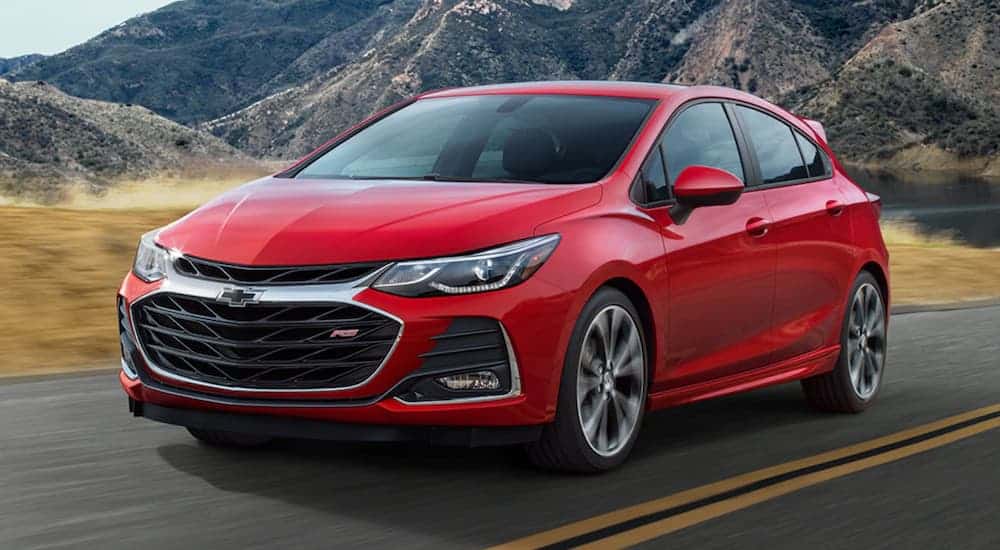 A red 2020 Chevy Sonic, which is a popular car at a Chevy dealer, is driving on a road with mountains in the background.