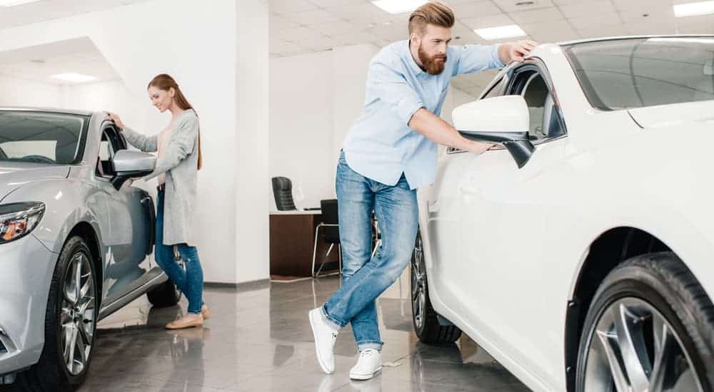A woman and man are looking at cars in a dealerships showroom. 