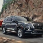 A dark grey 2020 Hyundai Palisade is towing a boat around a corner.