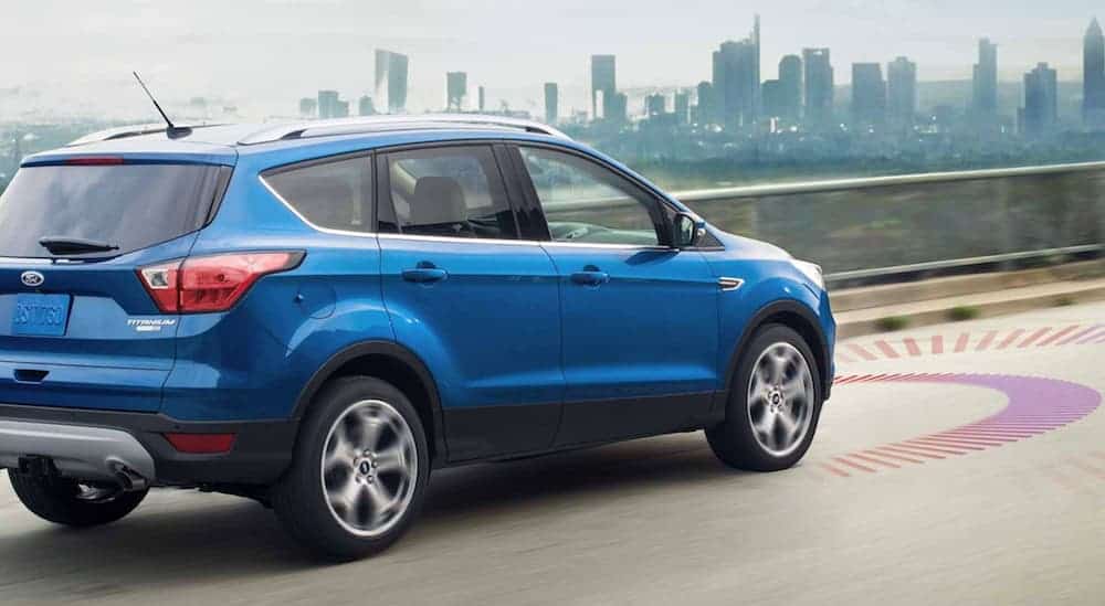 A blue 2019 Ford Escape is driving on the highway with the simulated Adaption Cruise Control visuals on the road.