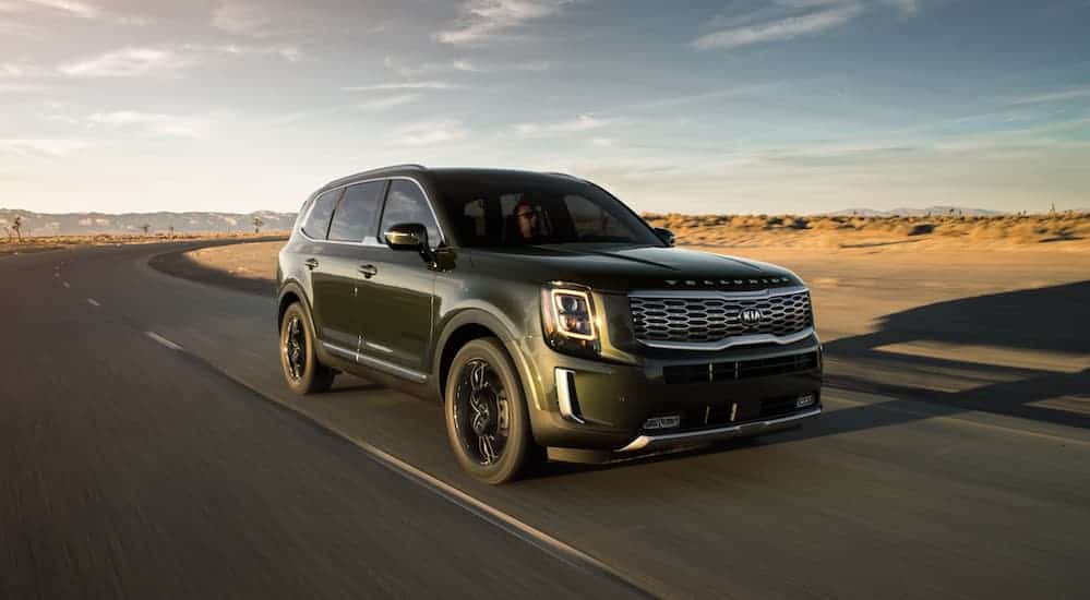 A green 2020 Kia Telluride, popular at local Kia dealership locations, is driving on a road through the desert. 