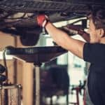 A mechanic is under a car performing an oil change.