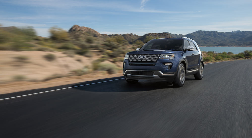 A blue 2018 Ford Explorer, which is a popular model when you search 'used cars for sale near me', is driving on a road with mountains in the background.