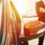A close up of a used car while a blurry salesman is in the background.