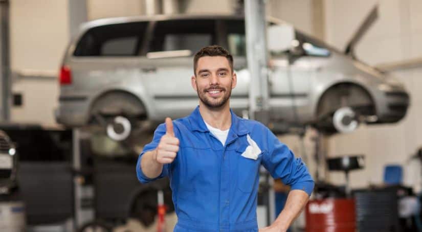A smiling mechanic is giving a thumbs up at a local car garage is shown.