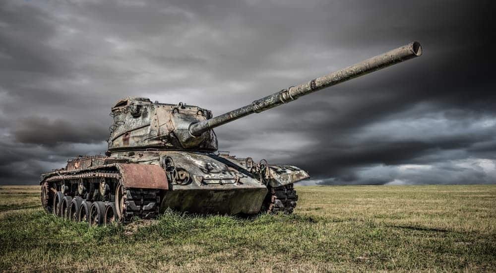A green World War 2 tank is parked in a grassy field with a dark sky in the background. 