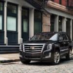 A black 2017 Cadillac Escalade, which is popular among used Cadillac's, is parked on a cobble stone road in front of a building.