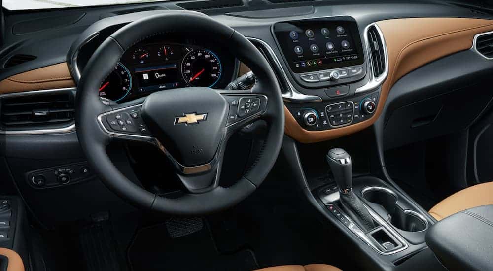 The black and brown leather interior of a 2020 Chevy Equinox is shown with an infotainment system and driver's display.