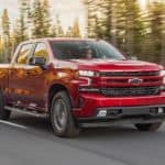 A red 2020 Chevy Silverado 1500, which wins when comparing the 2020 Chevy Silverado 1500 vs 2020 Ram 1500, is driving on a tree-lined road.