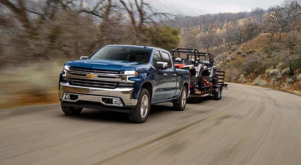 A blue 2020 Chevy Silverado 1500 is towing side-by-sides on a trailer uphill.