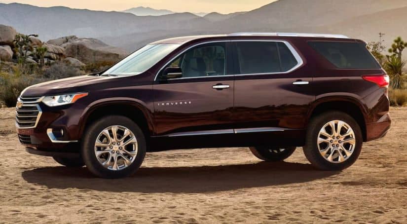 A burgundy 2020 Chevy Traverse is parked on sand with mountains in the background.