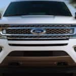 A white 2020 Ford Expedition is driving on a road shown from the front end.