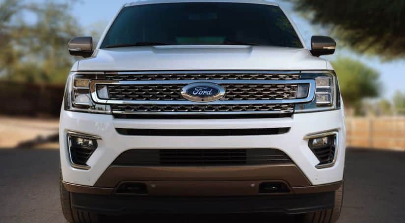 A white 2020 Ford Expedition is driving on a road shown from the front end.