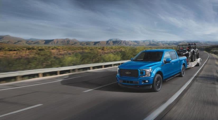 A blue 2020 Ford F-150, which wins when comparing the 2020 Ford F-150 vs 2020 GMC Sierra 1500, is towing side-by-sides on the highway.