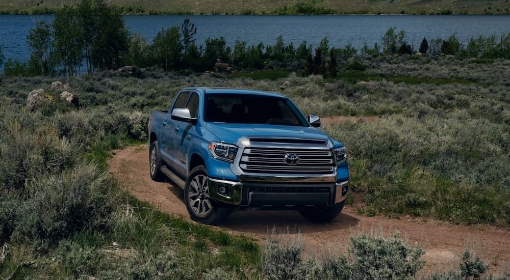 A blue 2020 Toyota Tundra is driving on a dirt road next to a lake. 