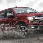 A red 2020 Ford F-150, which wins when comparing the 2020 Ford F-150 vs 2020 Toyota Tundra, is driving through a mud puddle.