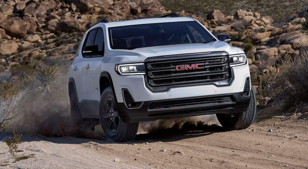 An all-new white 2020 GMC Acadia AT4 is driving on a dirt trail.